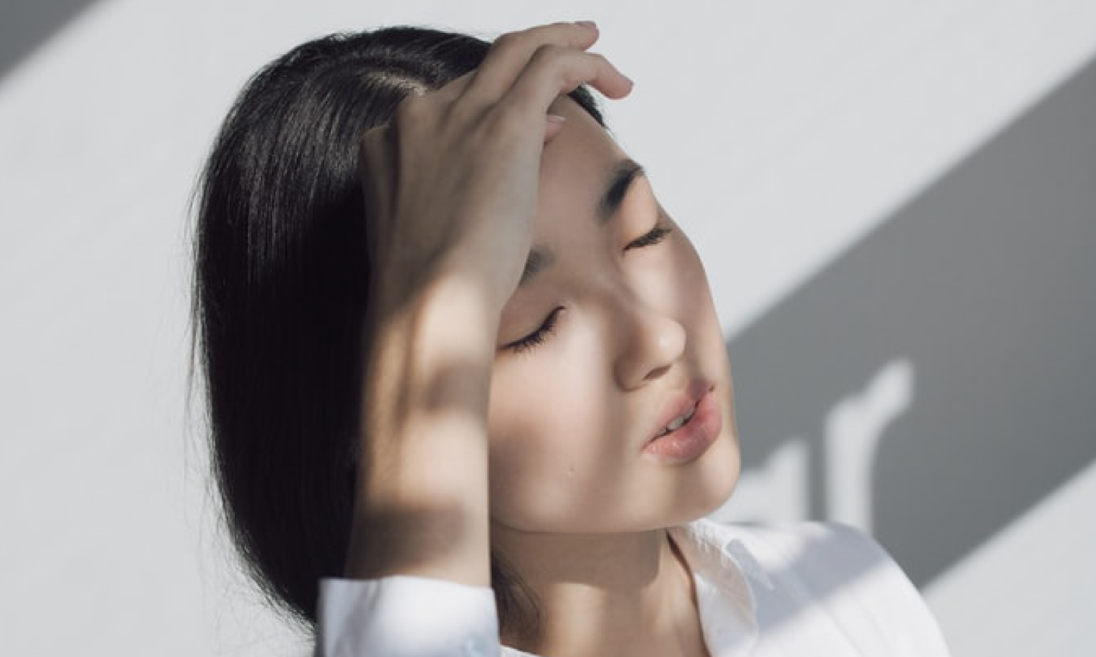 A young woman with short dark hair holds her hand to her forehead, with an exhausted face.